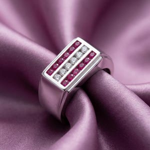 May include: A silver-toned ring featuring a rectangular face with three parallel channels. The outer two channels are set with small round red rubies, while the center channel contains a row of small round clear white diamonds.