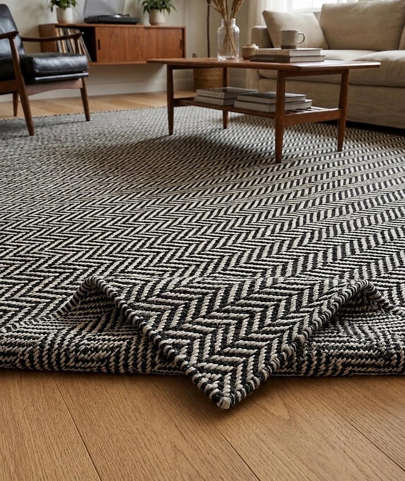 May include: A large area rug featuring a high-contrast black and white herringbone pattern woven with a thick, textured corded material. The rug is laid flat on a wooden floor with one corner folded over to reveal the underside and thickness.