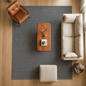 May include: A top-down view of a living room featuring a large black and white chevron rug, a tan leather armchair, a beige sofa with two matching throw pillows, a rectangular wooden coffee table with a small vase and book, and a beige ottoman.