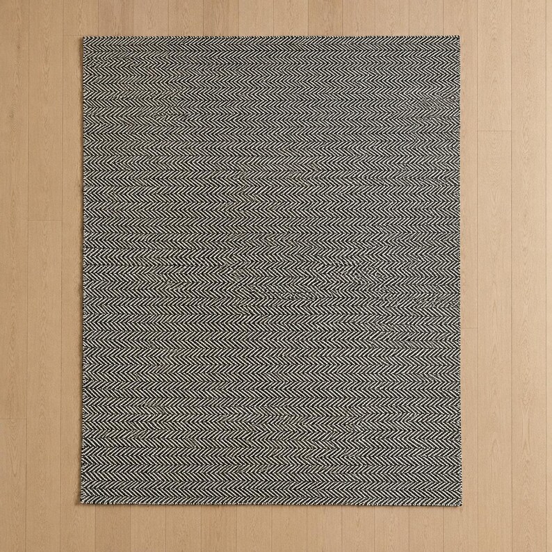 May include: A rectangular area rug featuring a dense, repeating black and white herringbone pattern. The woven textile displays a consistent zigzag texture across its entire surface, creating a high-contrast visual effect with sharp, clean lines.