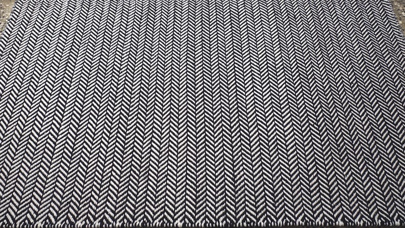 May include: A rectangular area rug featuring a high-contrast black and white herringbone pattern. The woven textile displays a repeating V-shaped chevron design that runs consistently across the entire surface of the floor covering.