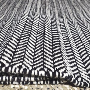 May include: A rectangular area rug featuring a high-contrast black and white herringbone pattern. The woven textile displays a repeating V-shaped chevron design across the entire surface, with one corner folded over to reveal the thickness of the rug.
