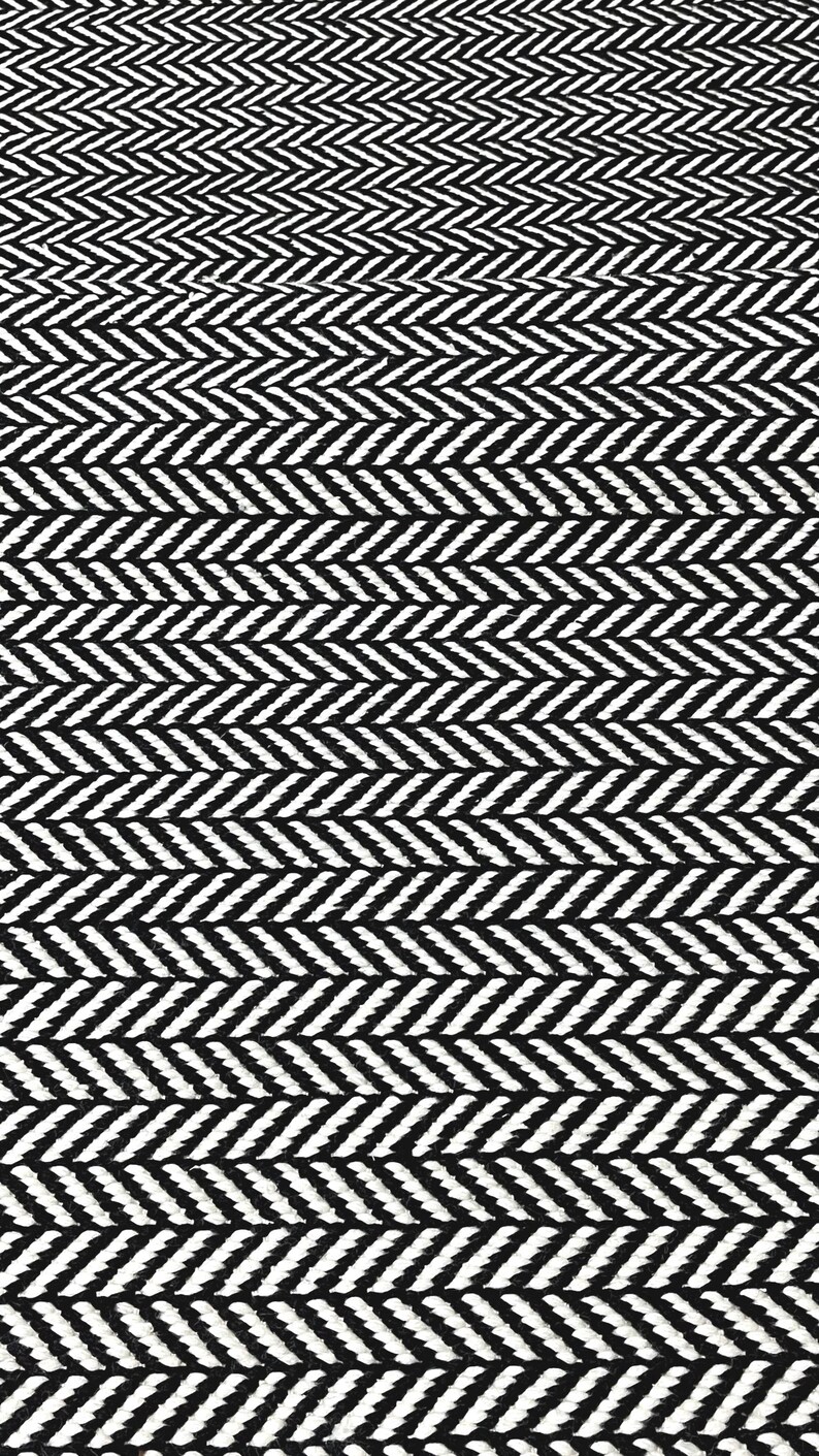 May include: A textile fabric featuring a high-contrast black and white herringbone pattern. The design consists of repeating V-shaped columns of woven threads that create a consistent, geometric zigzag texture across the entire surface area.