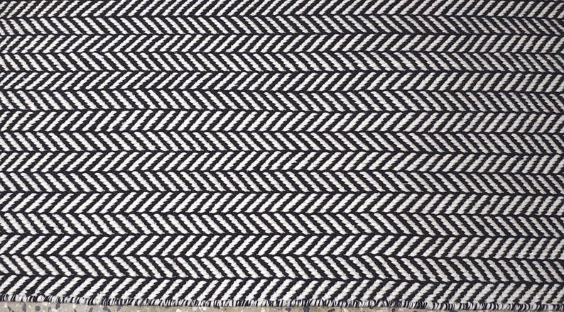 May include: A woven textile fabric featuring a repeating black and white herringbone pattern. The design consists of diagonal lines arranged in a V-shaped sequence across the entire surface, creating a consistent geometric texture throughout the material.