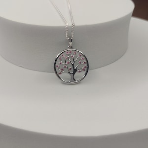 May include: A silver pendant necklace with a tree of life design. The circular pendant features a tree with pink gemstone leaves. The necklace hangs from a fine silver chain. The pendant's diameter is approximately 2.5 cm, making it a delicate piece of jewellery.