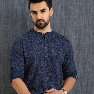 Pu&ograve; includere: Una camicia blu navy con un motivo geometrico. La camicia ha un colletto alla coreana e una chiusura con bottoni. Le maniche sono arrotolate. La persona indossa un orologio con quadrante bianco e cinturino blu.