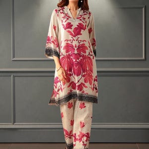 Puede incluir: Un conjunto de dos piezas compuesto por una túnica de manga larga y pantalones a juego. La túnica presenta un escote en V y un llamativo estampado de hojas magenta sobre un fondo crema, con un borde geométrico negro en el dobladillo.