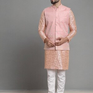 May include: A three-piece ensemble featuring a light pink Nehru jacket and a matching patterned tunic. The outfit is paired with white pants and dark brown slip-on shoes. The jacket has a mandarin collar.
