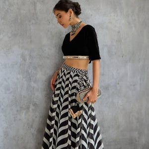 May include: A black velvet crop top with a V-neck and a gold embellished waistband paired with a flowing black and white chevron patterned skirt. A small gold clutch and matching wristlet complete the ensemble. The outfit is suitable for formal events.