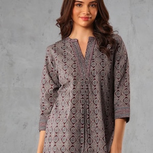 May include: A three-quarter sleeve tunic top with a V-neck. The top features a repeating floral pattern in shades of burgundy, gray, and white. The neckline and sleeve cuffs have striped detailing. The top is made of a soft, flowing fabric.