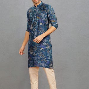 May include: A teal kurta with a floral pattern, paired with cream-colored pants. The kurta features a mandarin collar and button-down front. The outfit is completed with brown leather sandals. The overall style is a blend of traditional and contemporary fashion.