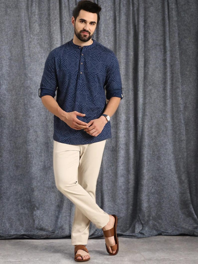 Pu&ograve; includere: Una camicia blu navy a maniche lunghe con un motivo geometrico, abbinata a pantaloni beige e sandali marroni. La camicia ha un colletto alla coreana e una chiusura con bottoni. I pantaloni sono a gamba dritta. I sandali sono in pelle.