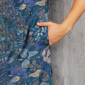 May include: Teal-colored dress with a floral pattern in shades of blue, gray, and gold. The dress features a pocket and a three-quarter sleeve. The fabric has a soft, flowing appearance.