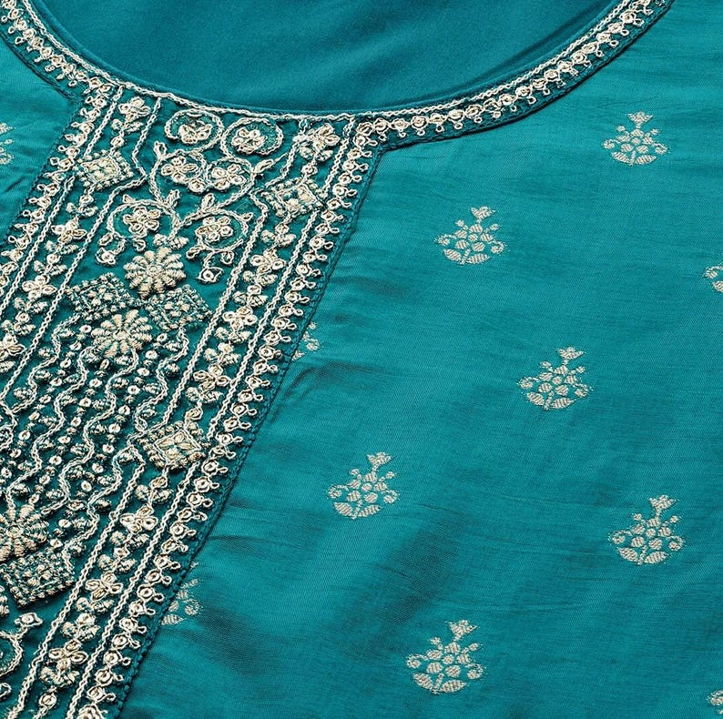 May include: Teal-colored garment with intricate embroidery around the neckline and down the front. The embroidery is a mix of floral and geometric patterns in a light, contrasting color. The fabric has a subtle sheen and small, repeating floral motifs.
