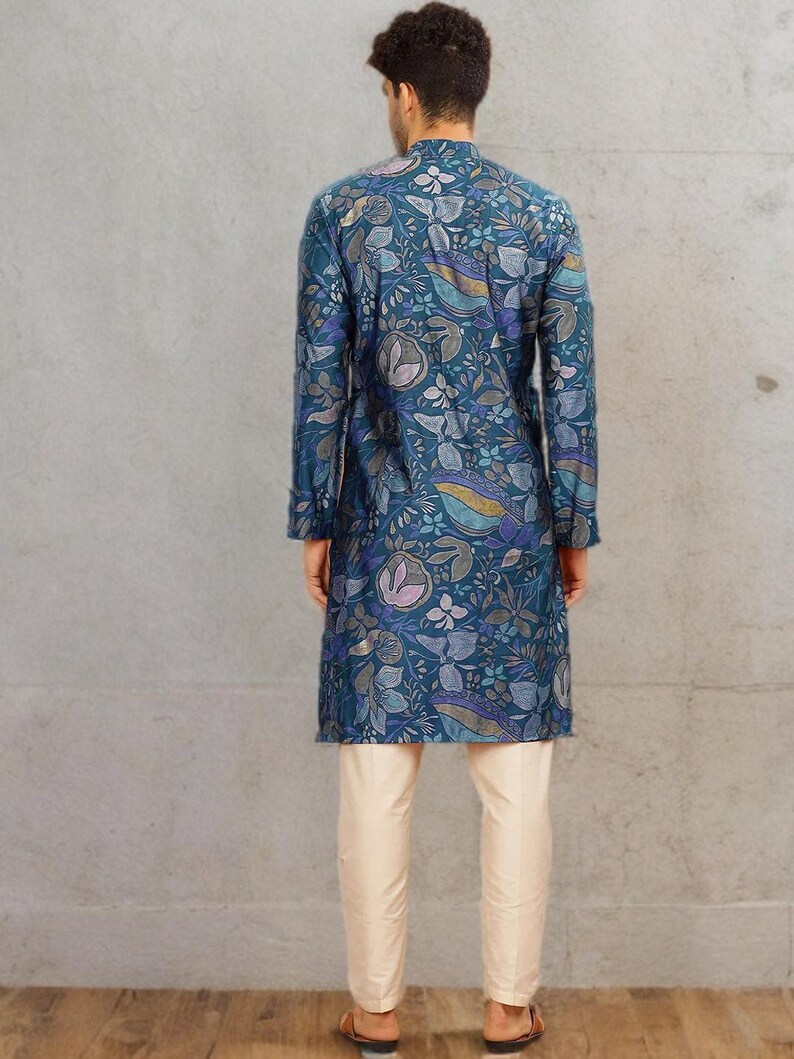 May include: A teal long-sleeved tunic with a floral pattern, paired with cream-colored pants. The tunic features a mandarin collar and a button-down front. The floral design includes shades of blue, purple, and gold. The pants are a straight-leg style.