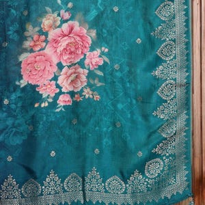 May include: Teal fabric with a floral design featuring large pink peonies and smaller peach-colored flowers. The fabric has a decorative border with a gold pattern and a tassel.