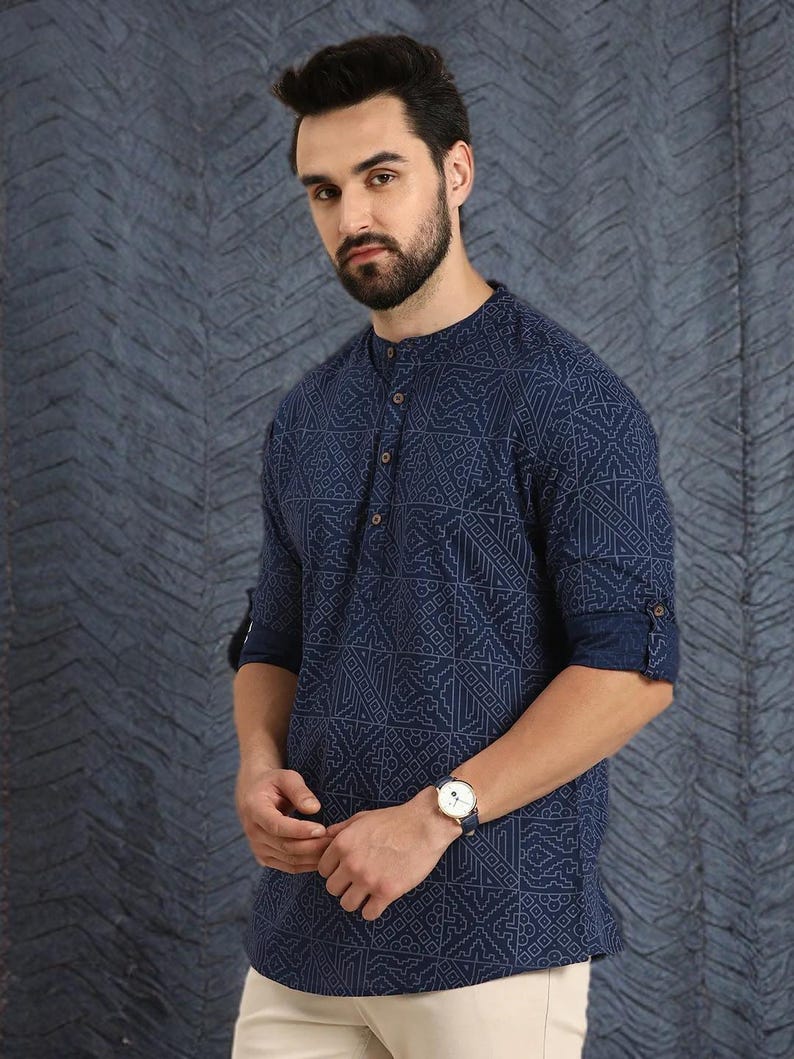 Pu&ograve; includere: Una camicia blu navy con motivo geometrico e colletto alla coreana. La camicia ha maniche lunghe arrotolate sui gomiti. &Egrave; visibile un orologio da polso con cinturino blu. La camicia &egrave; abbinata a pantaloni beige.