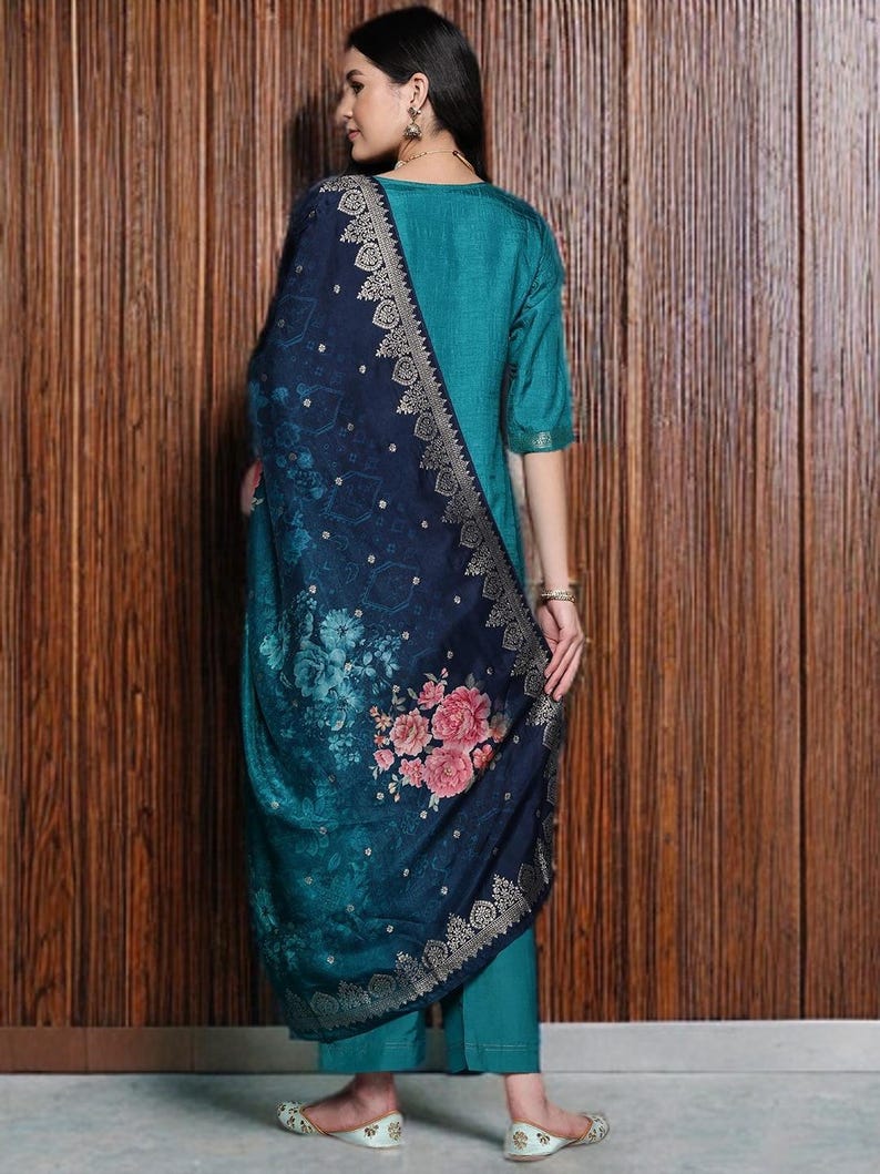 May include: A teal-colored, three-quarter sleeve outfit with matching pants. A dark blue shawl with a floral pattern and gold trim is draped over the shoulders. The outfit is worn with embellished flats.