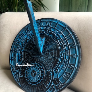 Könnte beinhalten: Eine blaue und schwarze Sonnenuhr mit römischen Ziffern und dem Text "COUNT NONE BUT HOURS, HORAS NULLUS NISI". Die Sonnenuhr hat ein Kompassrosen-Design und einen Gnomon. Die Sonnenuhr ist aus Metall und hat ein gealtertes Aussehen.
