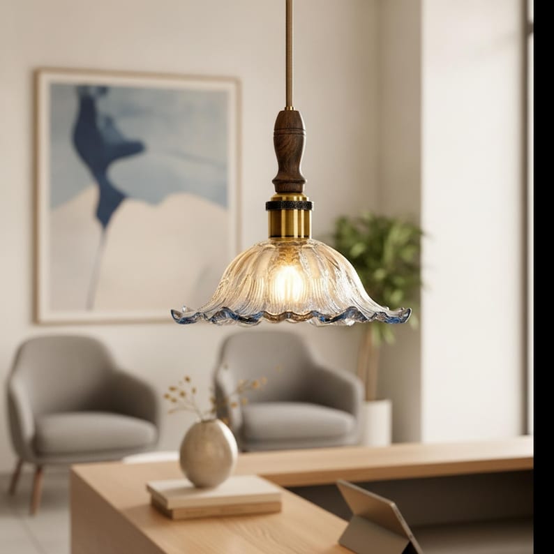 May include: A pendant light fixture featuring a fluted, clear glass shade with a subtle blue-tinted scalloped edge. The shade is attached to a dark wood handle and a brass-colored metal fitting, suspended by a thin, straight brass rod.