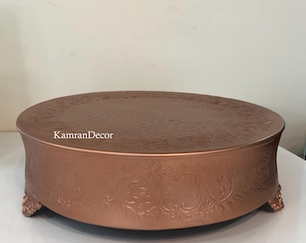 May include: A copper-colored cake stand with a round top and ornate floral detailing. The stand has a textured surface and is supported by decorative feet. The text "KamranDecor" is visible on the side.