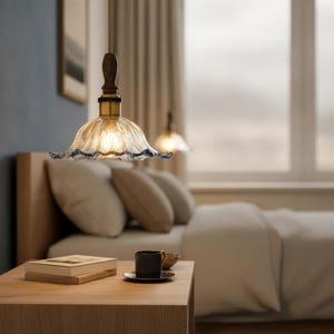 May include: A pendant light fixture featuring a fluted, clear glass shade with a scalloped edge, suspended by a dark wood handle and a brass-toned metal fitting. The light emits a warm glow, illuminating the textured glass surface.
