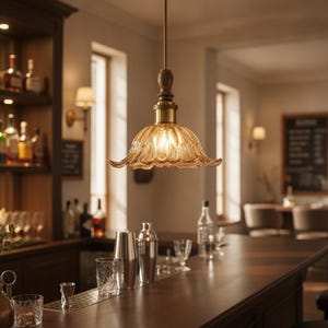 May include: A pendant light fixture featuring a scalloped, amber-tinted glass shade with a textured, petal-like pattern. The shade is suspended by a dark metal rod and a brass-toned socket, emitting a warm, soft glow from the internal bulb.