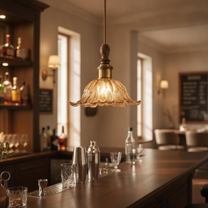 May include: A pendant light fixture featuring a scalloped, amber-tinted glass shade with a textured, petal-like pattern. The shade is suspended by a dark metal rod and a brass-toned socket, emitting a warm, soft glow from the internal bulb.