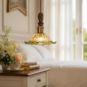 May include: A pendant light fixture featuring a scalloped, translucent green glass shade with a brass-toned metal socket and a dark brown, turned wood accent piece at the top, suspended by a thin, braided brown cord from the ceiling.
