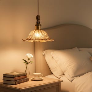 May include: A hanging pendant light fixture featuring a scalloped, amber-tinted glass shade with a fluted design. The light is suspended by a thin cord attached to a dark, textured wooden mount and a metallic gold-toned hardware connector.