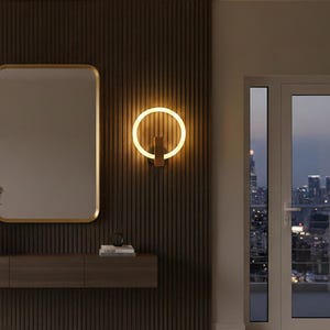 May include: A modern interior scene featuring a rectangular mirror with a gold frame and a circular wall sconce with a warm, glowing light. The wall is a dark brown with vertical paneling, and a wooden console table is below the mirror.