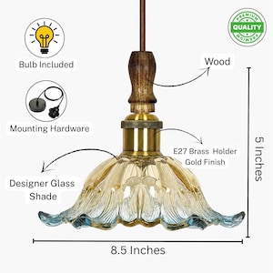 May include: A pendant light featuring a scalloped designer glass shade with amber and blue tones, a gold finish E27 brass holder, and a wood accent piece. The fixture measures 5 inches in height and 8.5 inches in width, including mounting hardware.