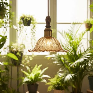 May include: A pendant light fixture featuring a scalloped, amber-tinted glass shade with a fluted petal design. The shade is attached to a dark wood-toned neck and a brass-colored metal socket, suspended by a thin cord from the ceiling.