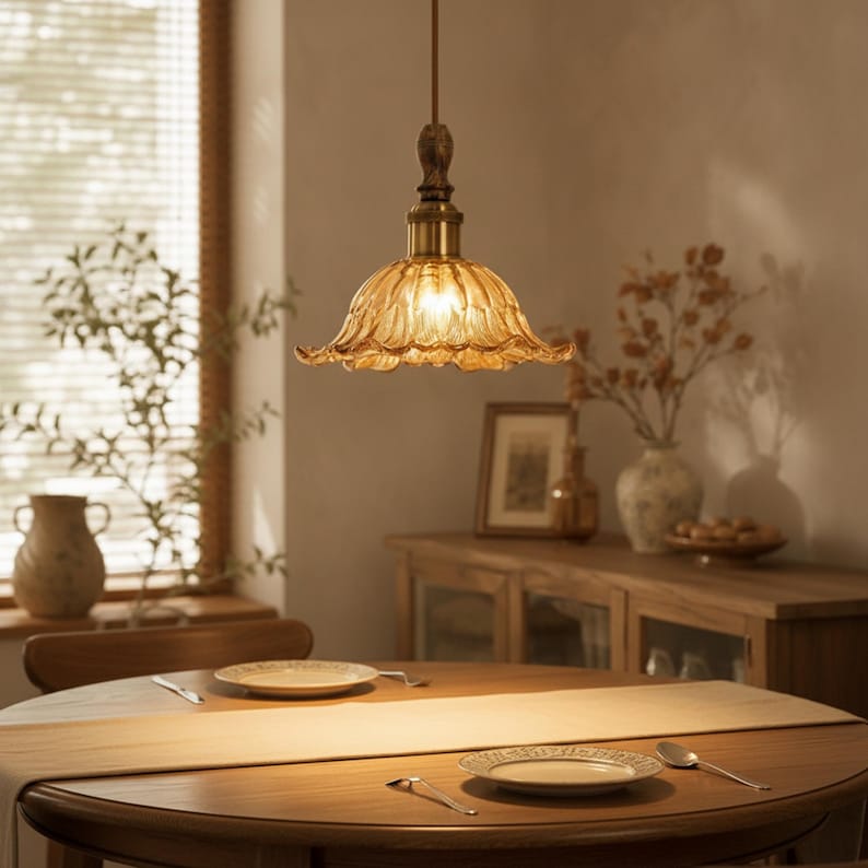 May include: A pendant light fixture featuring a scalloped, amber-colored glass shade with a ribbed texture. The lamp is suspended by a thin cord and includes a metallic brass-toned hardware fitting at the top, emitting a warm, soft glow.