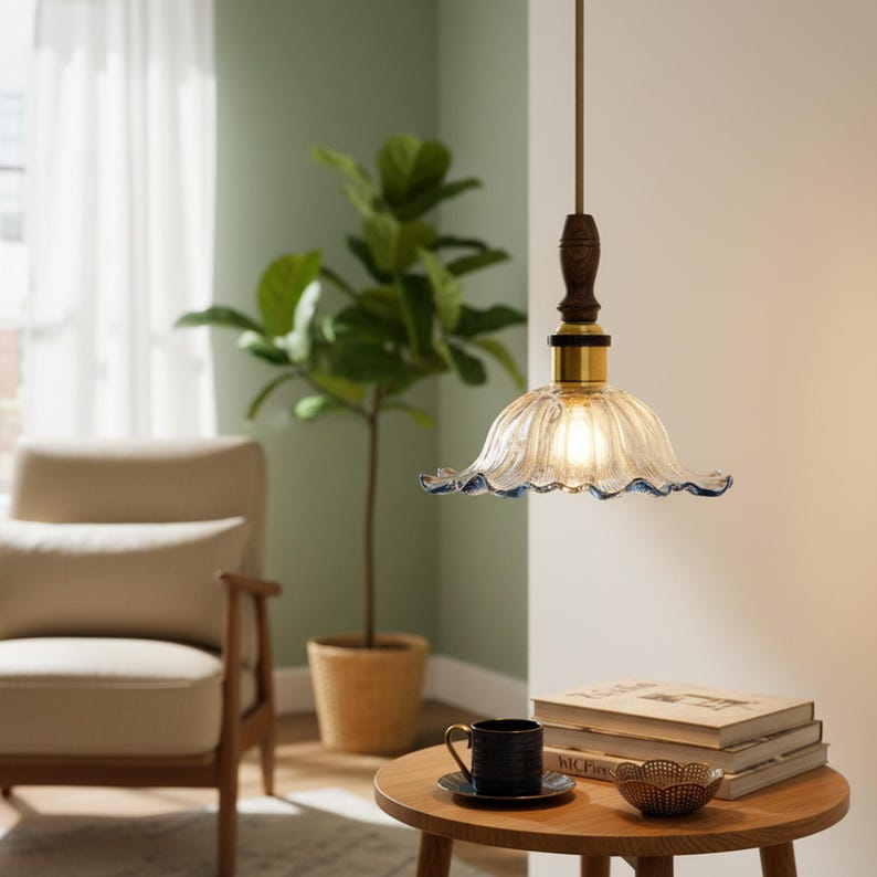 May include: A pendant light fixture featuring a clear, fluted glass shade with a ruffled, blue-tinted edge. The shade is attached to a dark wood neck and a brass-toned metal fitting, suspended by a thin cord from the ceiling above a wooden table.