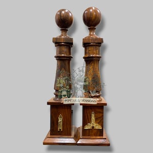 May include: Two decorative wooden pillars with a dark brown finish. Each pillar features a spherical top, a detailed central section with green and gold accents, and a square base with gold embellishments. The text "PIPERS & MASONS" is visible.