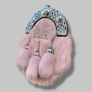 May include: A pink fur sporran with a silver Celtic design cantle. The sporran has three matching fur tassels with silver metal accents. The text "PIPERS & MASONS" is visible on the front.