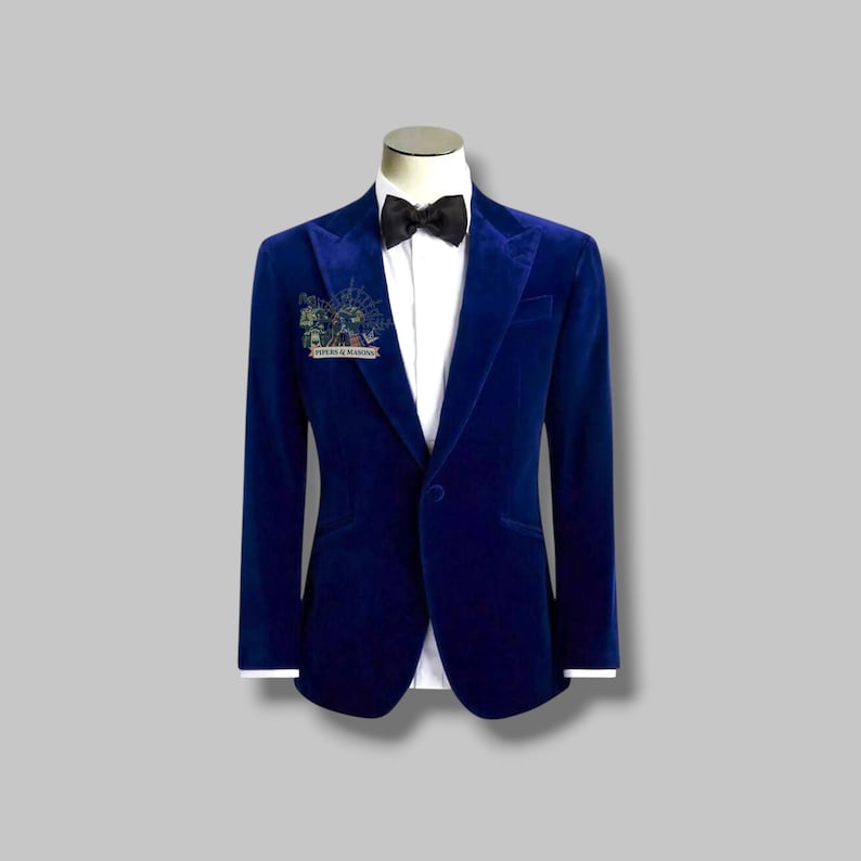 May include: A vibrant blue velvet blazer with a black bow tie and a white dress shirt. The blazer has a single-button closure and a small pin on the lapel. The pin has the text "PIPERS & MANSON".