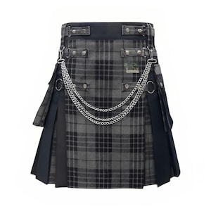 Puede incluir: Un kilt a cuadros grises y negros con detalles de cadena plateada. El kilt presenta un diseño plisado, una cinturilla negra y herrajes metálicos decorativos. Un pequeño parche con texto es visible en la parte delantera.