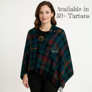 May include: A green, blue, and red plaid shawl with a decorative brooch. The shawl has a fringed edge and a crest emblem. Text in the image reads "Available in 50+ Tartans."