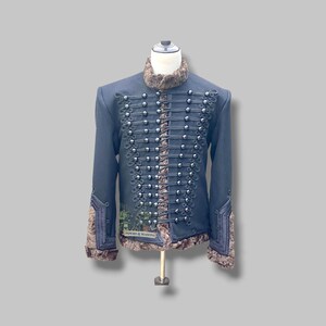 May include: A navy blue military-style jacket with silver-colored buttons and trim. The jacket features a faux fur collar and cuffs. The text "PIPERS & MASONS" is visible on the lower left side of the jacket.
