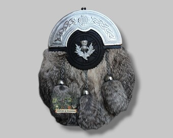 Puede incluir: Un sporran escocés tradicional con un cantle plateado con nudos celtas. El sporran tiene un cuerpo de piel, una solapa de cuero negro con un emblema de cardo y borlas decorativas. La etiqueta inferior dice "Pipers & Masons."