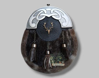 May include: A traditional Scottish sporran with a fur body and a decorative silver metal top. The sporran features a black leather front with a gold-coloured stag head emblem. Tassels hang from the bottom, and the text "PIPERS & MASONS" is visible.