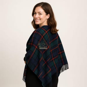 May include: A navy, green, and red plaid shawl with fringe. The shawl has a square patch with the text "PIPERS & MASONS" and a tree design. The shawl is draped over the shoulders.