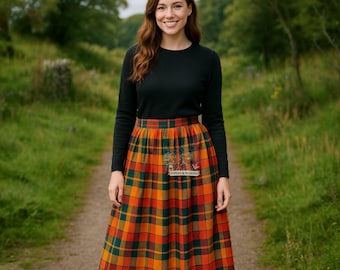 May include: A long-sleeved black crewneck sweater paired with a high-waisted, pleated midi skirt featuring a vibrant plaid pattern in shades of orange, red, green, and yellow. A small rectangular label with the text Pipers & Masons is visible.