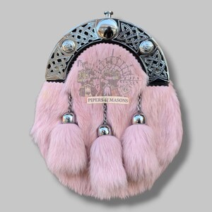 May include: Pink fur sporran with a silver Celtic design on the top and three matching tassels. The sporran has a silver clasp and chain. The text "PIPERS & MASONS" is printed on the front.