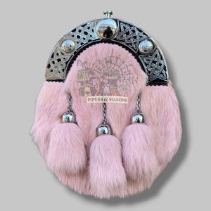 May include: Pink fur sporran with a silver Celtic design on the top and three matching tassels. The sporran has a silver clasp and chain. The text "PIPERS & MASONS" is visible on the front.