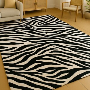 Op de afbeelding: Een groot rechthoekig tapijt met een opvallend zebra streepmotief in zwart en crème. Het tapijt ligt op een lichtgekleurde houten vloer en de kamer heeft een neutraal kleurenpalet. Het tapijt voegt een opvallend contrast toe aan de inrichting van de kamer.