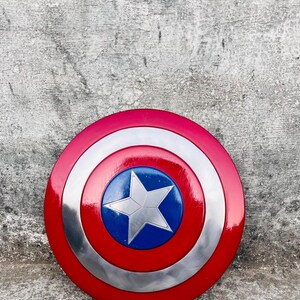 May include: A round shield with a red, white, and blue color scheme. The shield has a red outer ring, a silver middle ring, and a blue center with a white star. The shield is a replica of Captain America's shield.