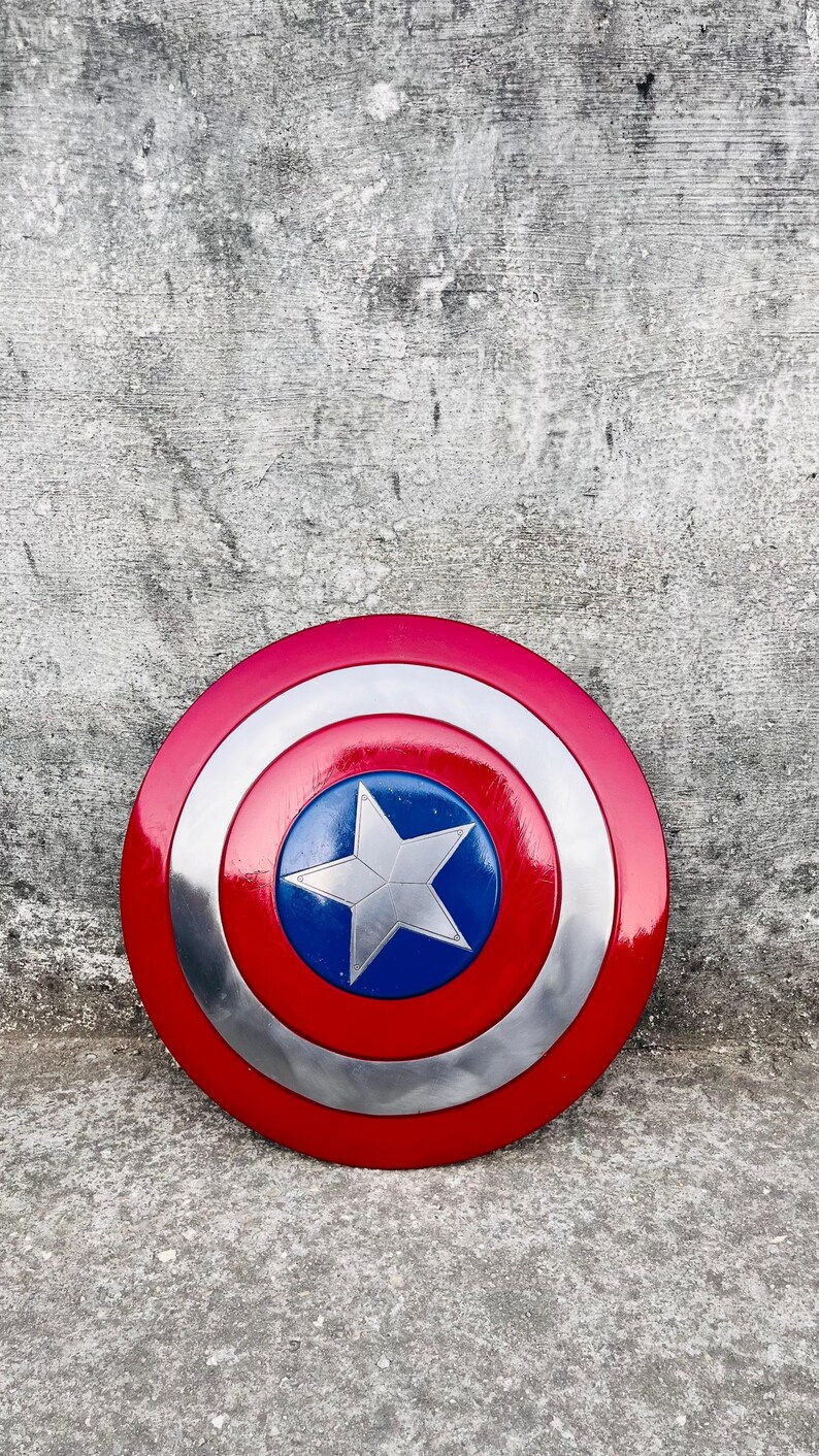May include: A round shield with a red, white, and blue color scheme. The shield has a red outer ring, a silver middle ring, and a blue center with a white star. The shield is a replica of Captain America's shield.